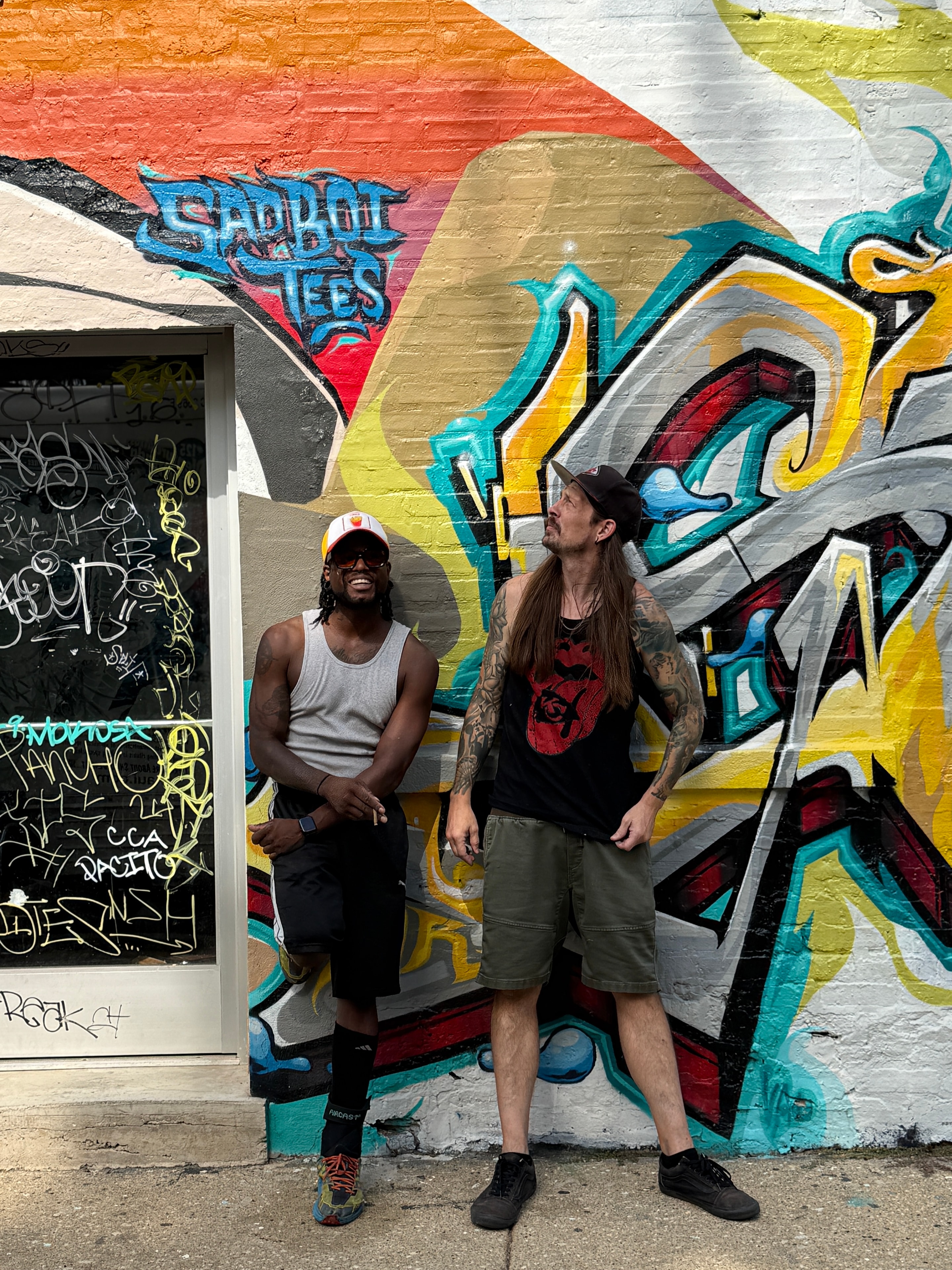 Sad Boi Tees founders laughing in front of the mural — Chicago